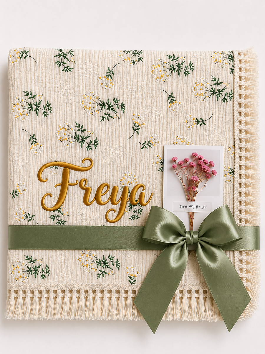 Camomile floral muslin blanket personalised with Freya in gold embroidery, with cream fringe and olive-green ribbon.