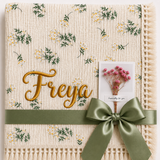Camomile floral muslin blanket personalised with Freya in gold embroidery, with cream fringe and olive-green ribbon.