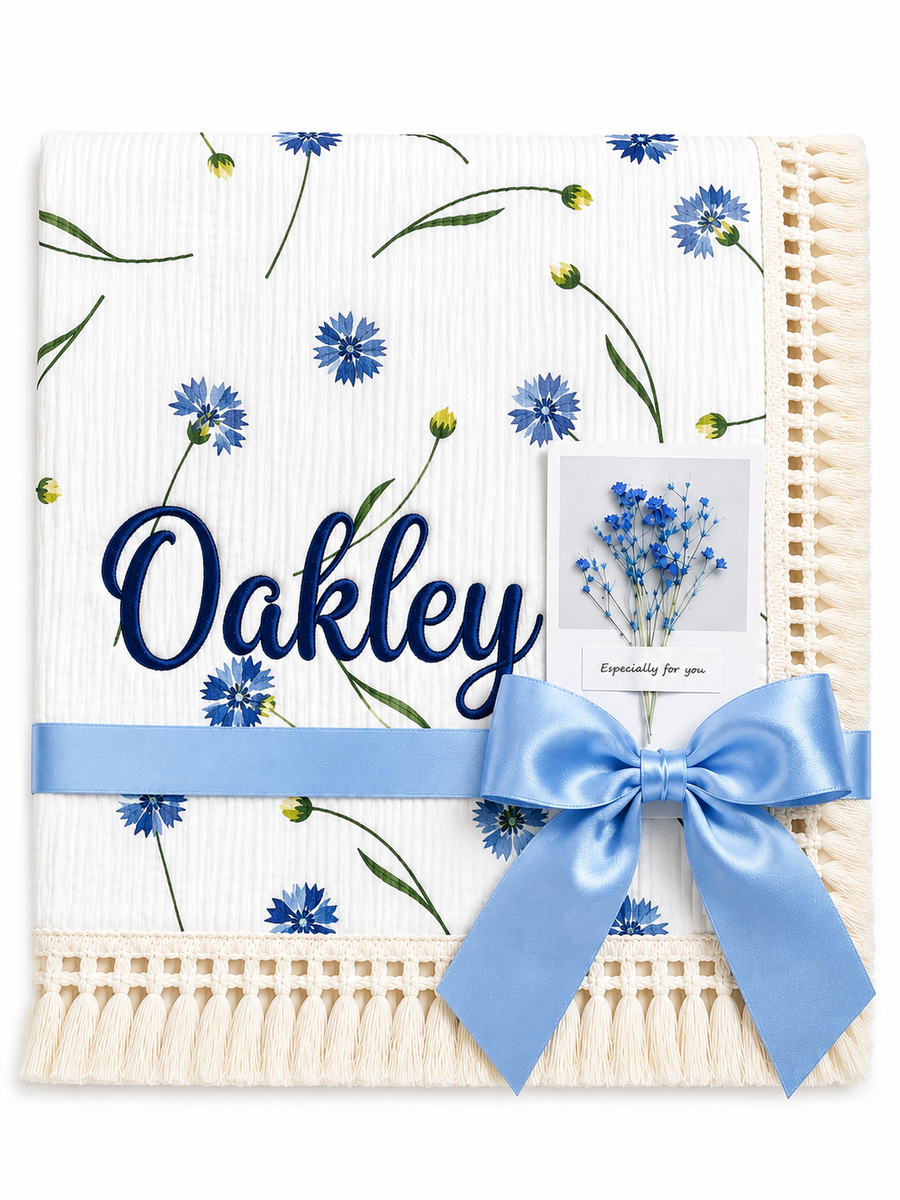 Cornflower Meadow muslin baby blanket with blue flowers, Oakley embroidered in navy, cream fringe and blue ribbon.
