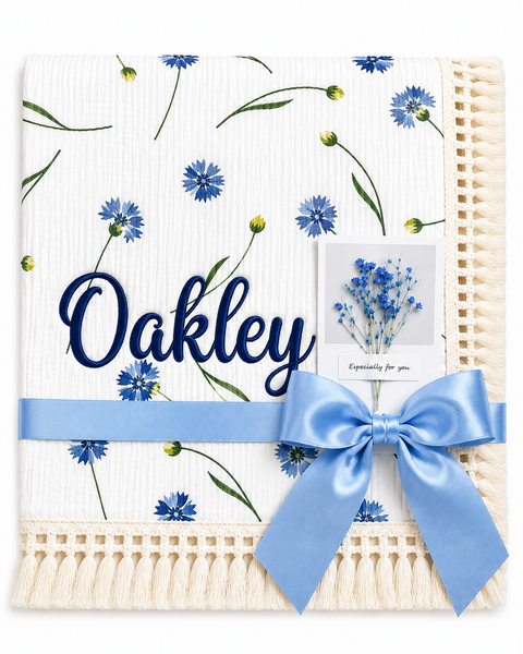 Cornflower Meadow muslin baby blanket with blue flowers, Oakley embroidered in navy, cream fringe and blue ribbon.