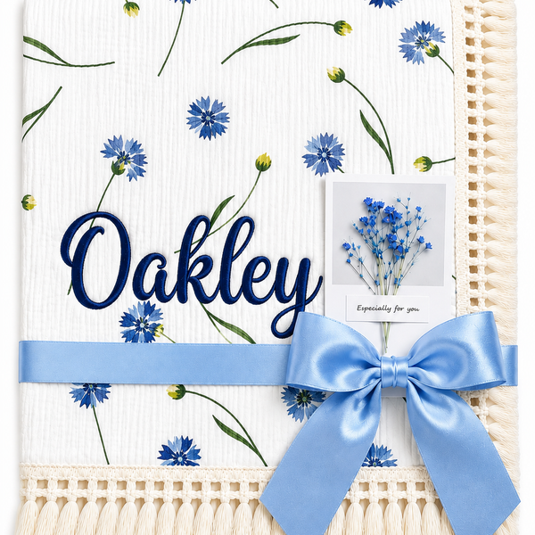 Cornflower Meadow muslin baby blanket with blue flowers, Oakley embroidered in navy, cream fringe and blue ribbon.