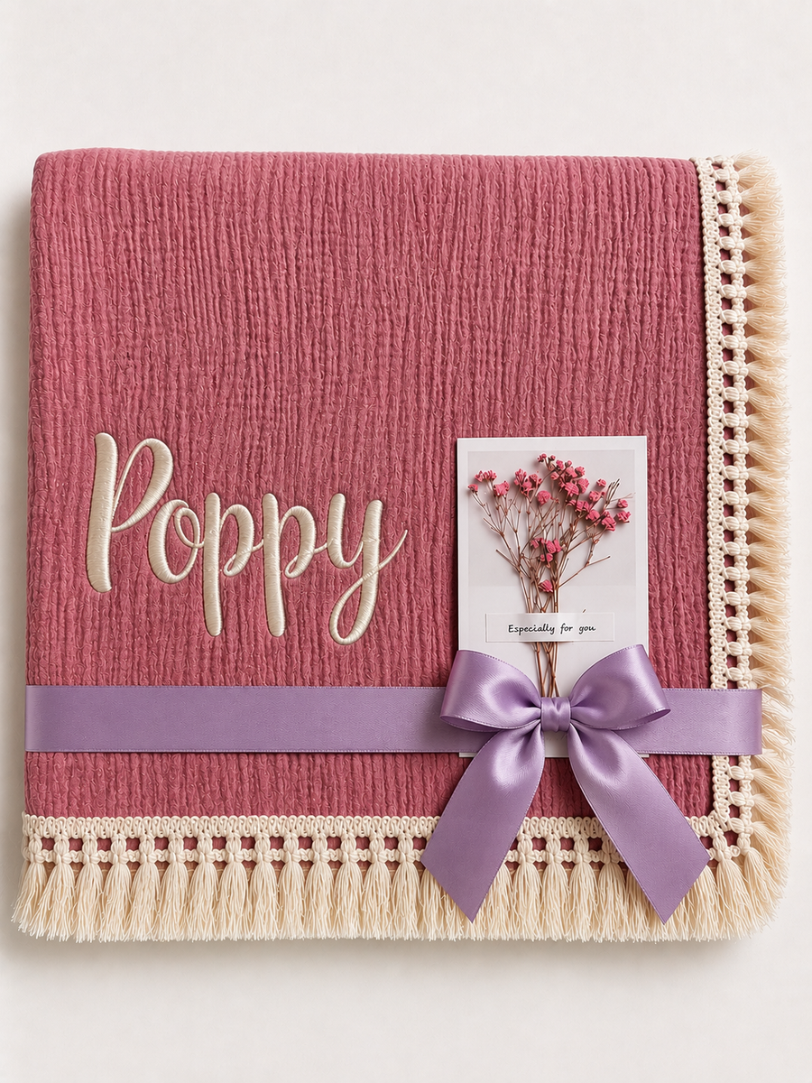 Dusty Pink muslin baby blanket personalised with Poppy in cream embroidery, a fringed border and lilac ribbon.