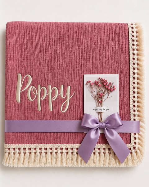 Dusty Pink muslin baby blanket personalised with Poppy in cream embroidery, a fringed border and lilac ribbon.