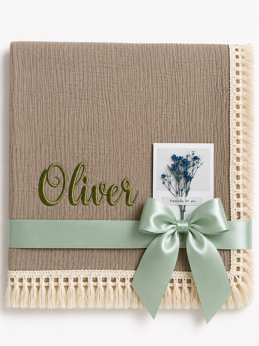 Taupe muslin baby blanket with Oliver embroidered in green, cream fringed edging and a mint ribbon.