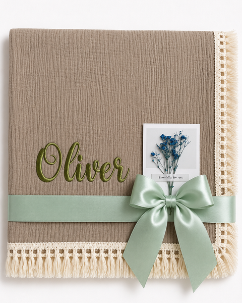 Taupe muslin baby blanket with Oliver embroidered in green, cream fringed edging and a mint ribbon.
