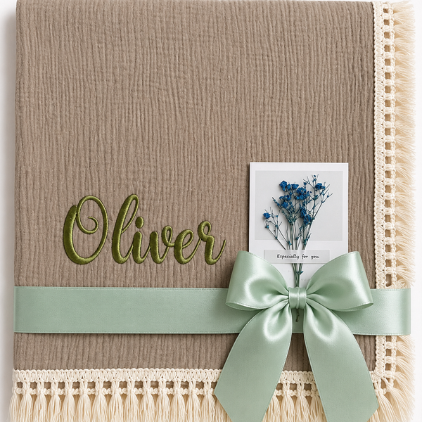Taupe muslin baby blanket with Oliver embroidered in green, cream fringed edging and a mint ribbon.