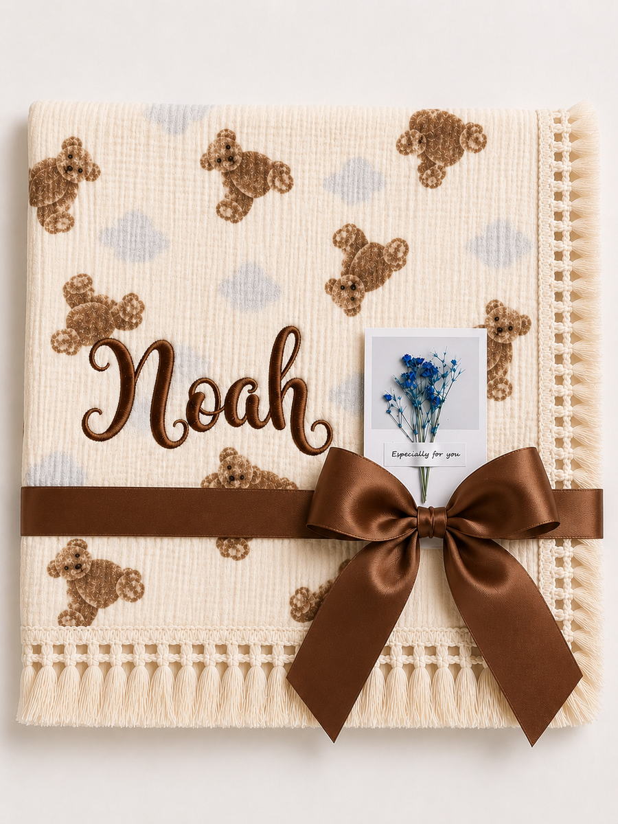 Cream teddy-print muslin baby blanket personalised with Noah embroidered in brown, with a fringed border.
