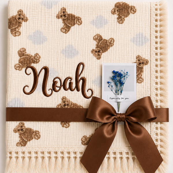 Cream teddy-print muslin baby blanket personalised with Noah embroidered in brown, with a fringed border.