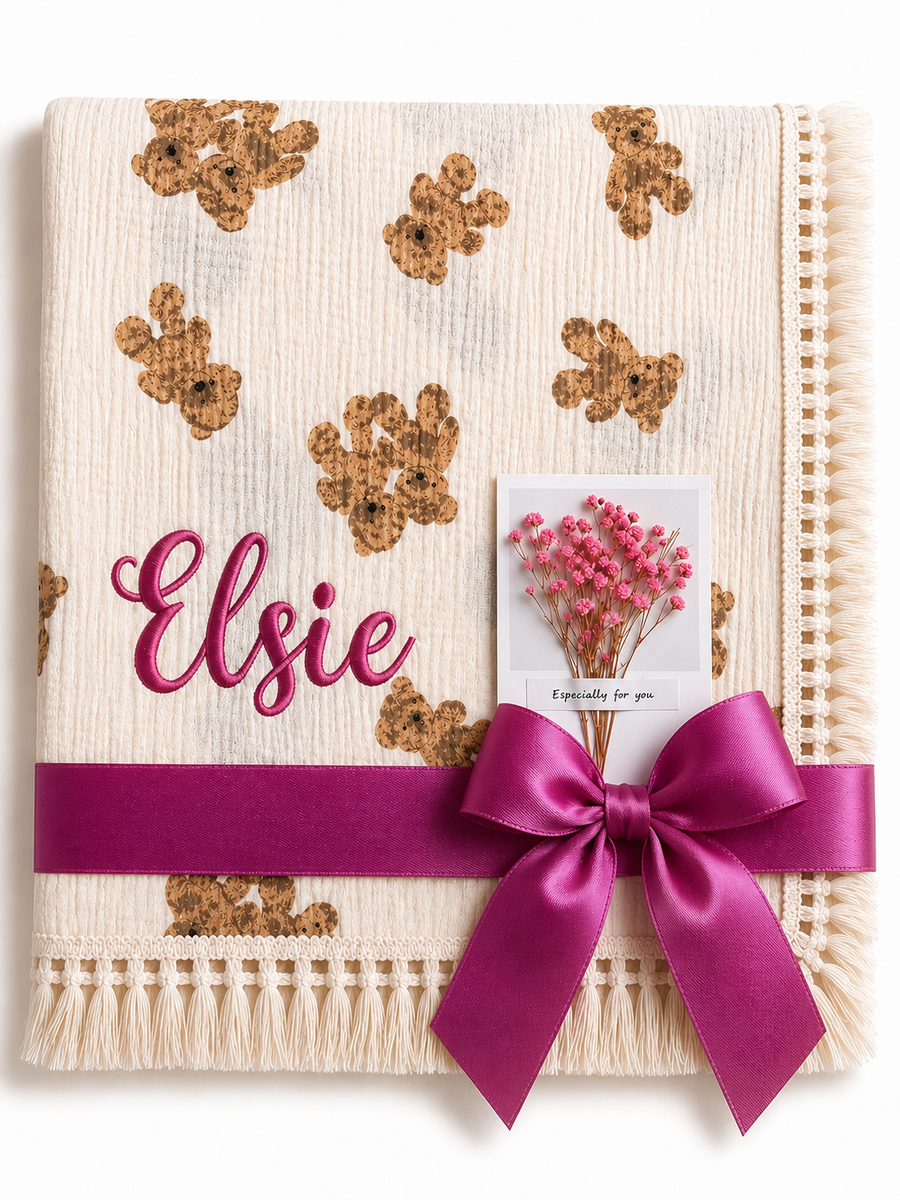 Cream Twin Bear muslin baby blanket with teddy-face print, Elsie embroidered in pink and a magenta ribbon.