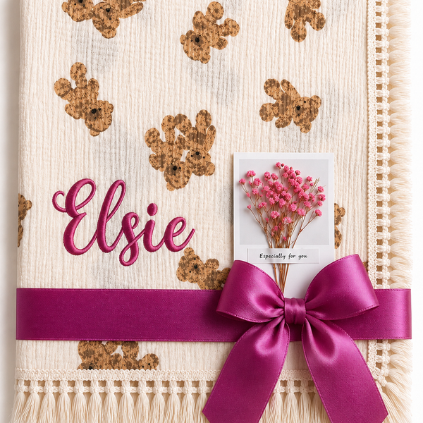 Cream Twin Bear muslin baby blanket with teddy-face print, Elsie embroidered in pink and a magenta ribbon.